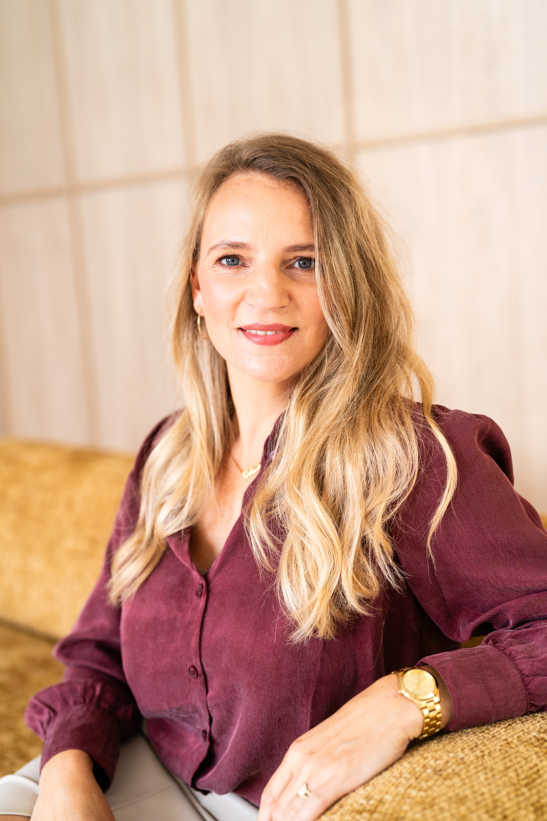 Marly in een bordeauxrode blouse met gouden sieraden, met een warmere uitstraling